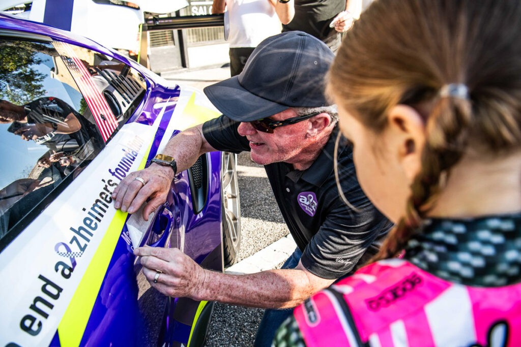 Mark Kvamme applies his grandfather's name to the No. 43 Porsche as a young fan watches.